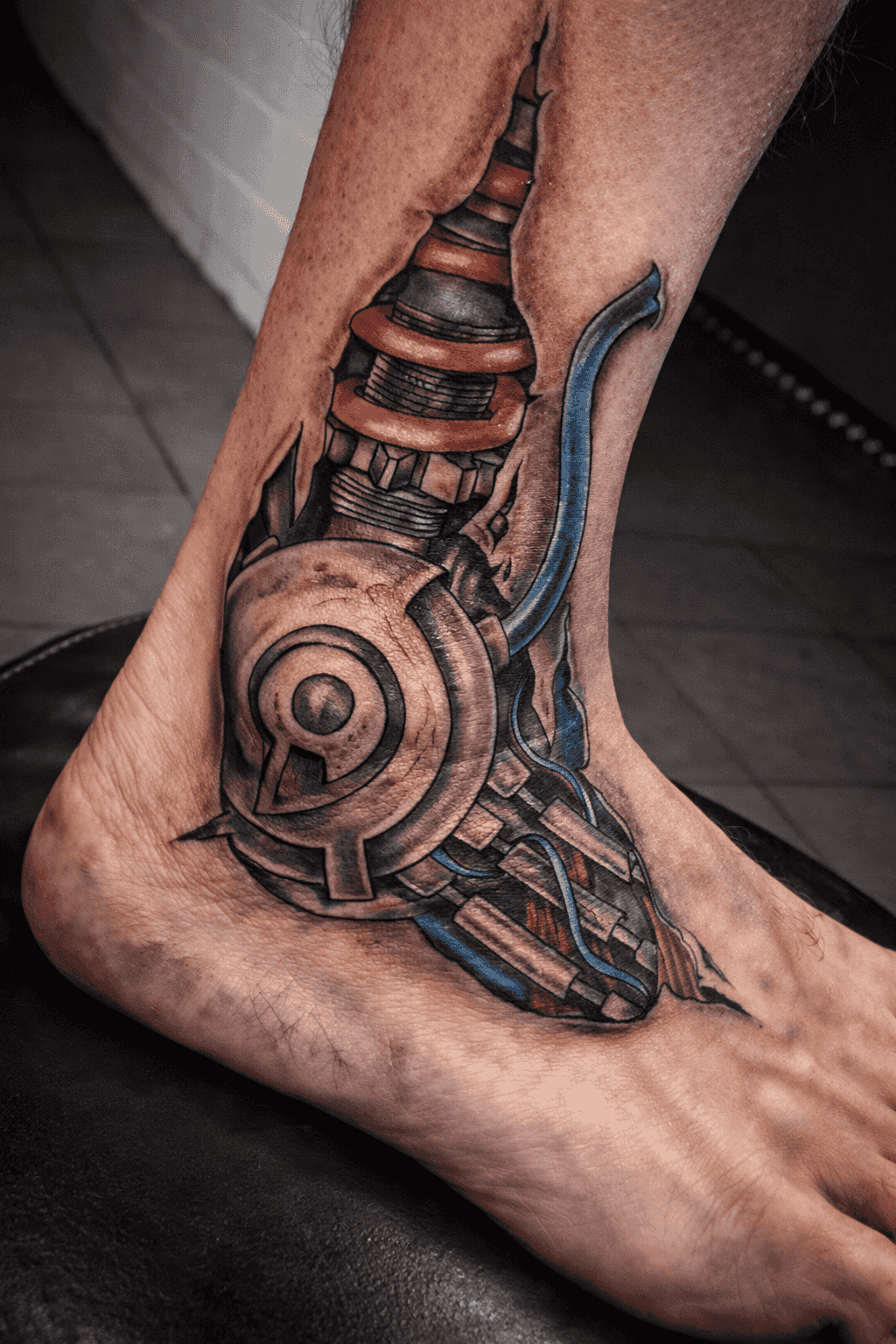 Tatouage biomécanique réaliste sur la jambe, représentant des pièces mécaniques intégrées dans la peau avec un ombrage et des textures très détaillés, réalisé par Steven Chaudesaigues au Bastia Tattoo, salon de tatouage à Bastia.