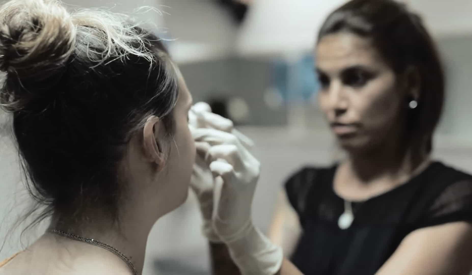 Nadia faisant un piercing sur le visage d'une jeune femme au studio graphicaderme orange